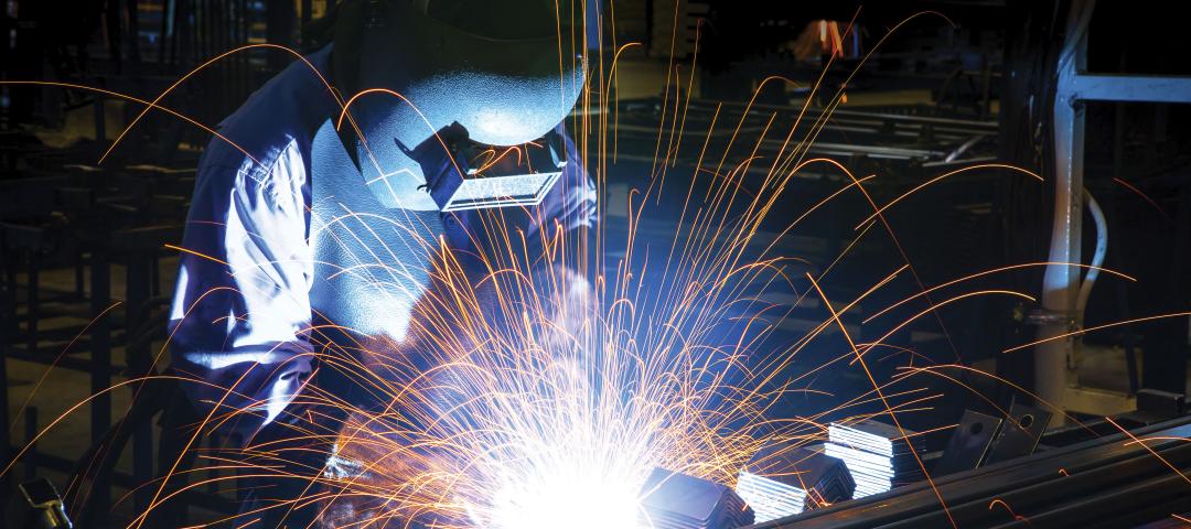 Welder operator clad in full protective gear joins metal together.